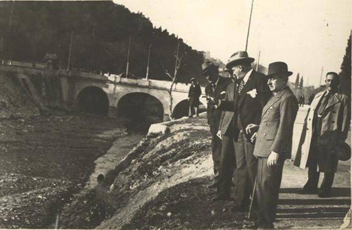 Αθήνα, 1937. Κάλυψη Ιλισού Ο Διοικητής Πρωτευούσης (επί δικτατορίας Μεταξά) Κωνσταντίνος Κοτζιάς επισκέπτεται τα έργα της κάλυψης Ιλισού μπροστά Στις αρχές του 20ου αιώνα ολόκληρη η περιοχή μεταξύ Ιλισού και Υμηττού είχε κηρυχθεί αναδασωτέα και είχε φυτευτεί. Στη δεκαετία του ’50 ολοκληρώθηκε η κάλυψη της κοίτης του ποταμού και τη θέση του ποταμού πήραν οι οδοί Μιχαλακοπούλου, Βασιλέως Κωνσταντίνου και Καλλιρόης. Το έργο είχε ξεκινήσει το 1939 και το θεμελίωσε ο Μεταξάς με τη χαρακτηριστική φράση : «Θάπτομεν τον Ιλισόν». Πηγή: Η Αθήνα μέσα στο χρόνο