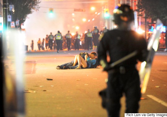 VANCOUVER, BC - JUNE 15: (EDITORS NOTE: Photo three of five, in sequence.) Riot police walk in the street as a couple kiss on June 15, 2011 in Vancouver, Canada. Vancouver broke out in riots after their hockey team the Vancouver Canucks lost in Game Seven of the Stanley Cup Finals. (Photo by Rich Lam/Getty Images)