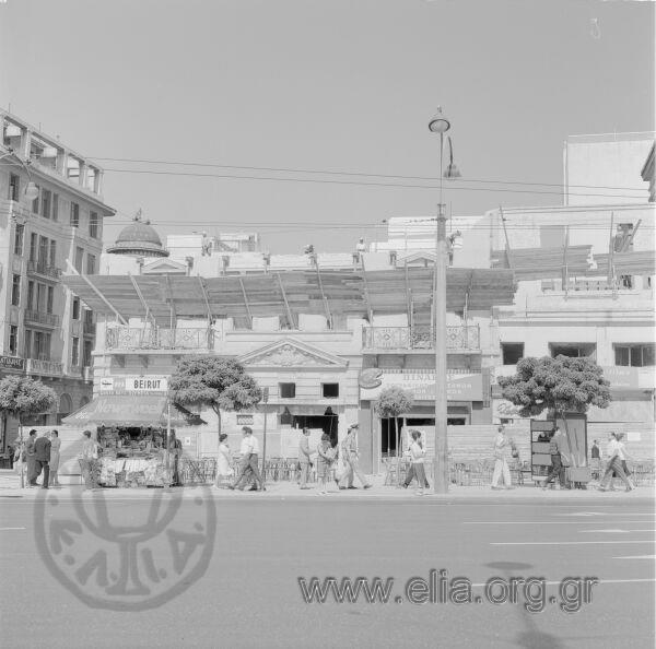 Αθήνα, Αύγουστος 1963. Σπάνιo τεκμήριο όπου απαθανατίζεται η κατεδάφιση του Μεγάρου Κωνσταντίνου Νικολούδη, που υπήρχε επί της Πλατείας Συντάγματος & Μητροπόλεως 2. Στο αρχικό διώροφο κτήριο που ήταν η οικία του Ανάργυρου Σιμόπουλου προστέθηκαν το 1925 δύο επιπλέον όροφοι και cartouche.