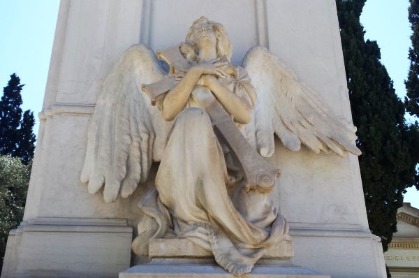 Ένας άγγελος που κρατά έναν μεγάλο σταυρό στα χέρια του και κοιτά τον ουρανό βρίσκεται στην αριστερή πλευρά του τάφου της οικογένειας του Πεσμαζόγλου